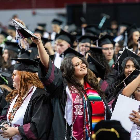 NMSU graduate holding their cap in the air after graduating